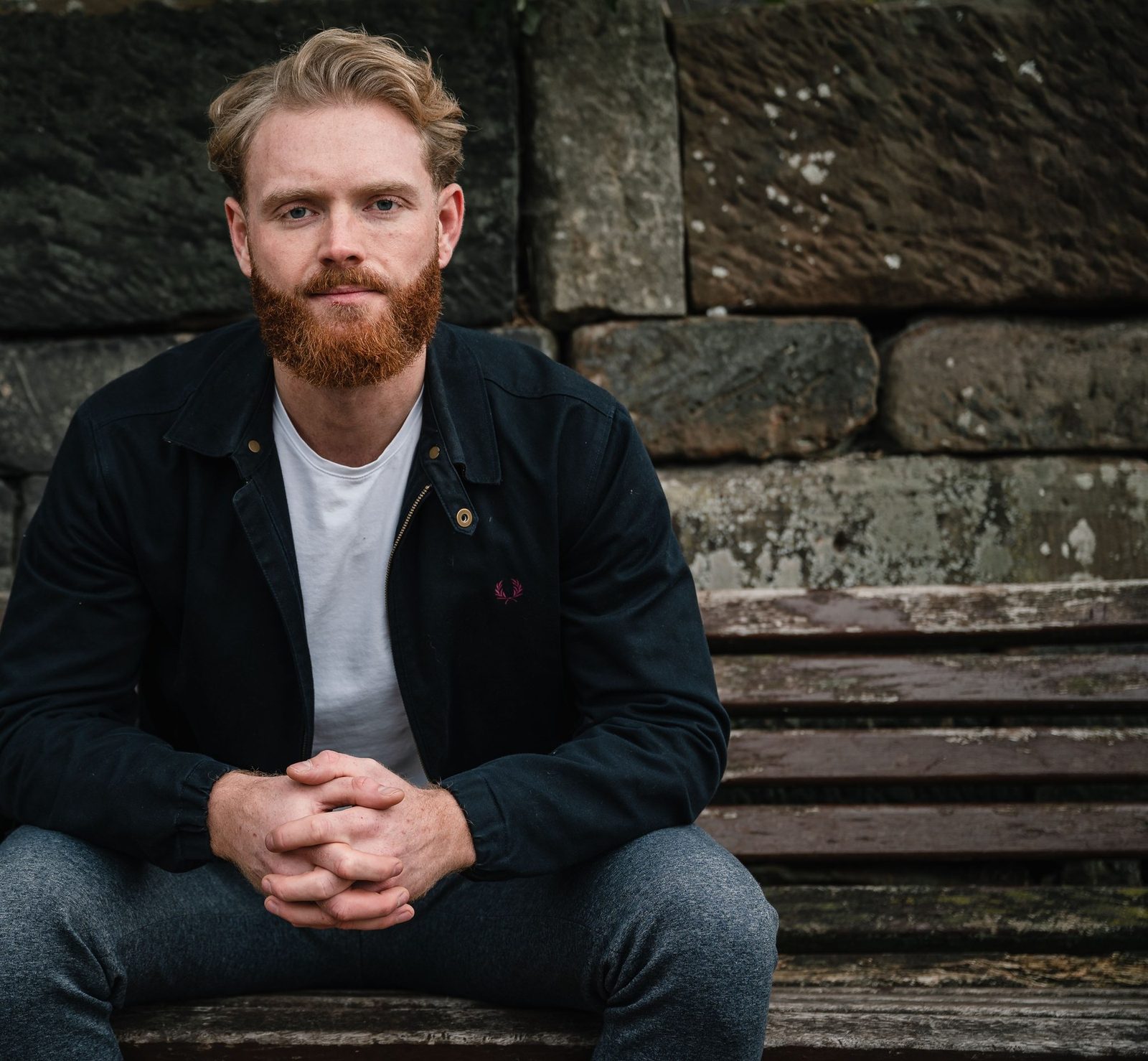 Dan Martin sitting on a bench against a stone wall in Castlefield