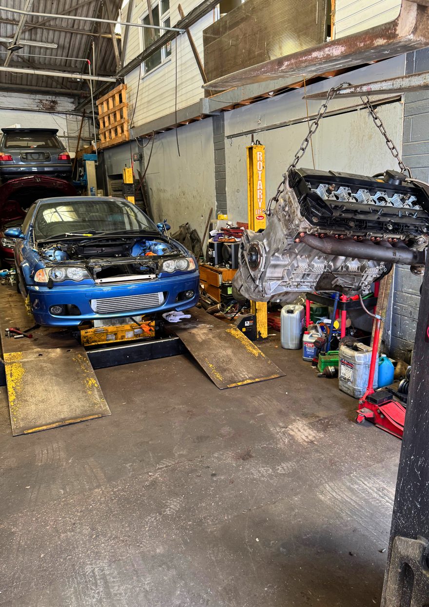 Dan's blue BMW 330Ci mid-restoration in a workshop, engine out on a hoist