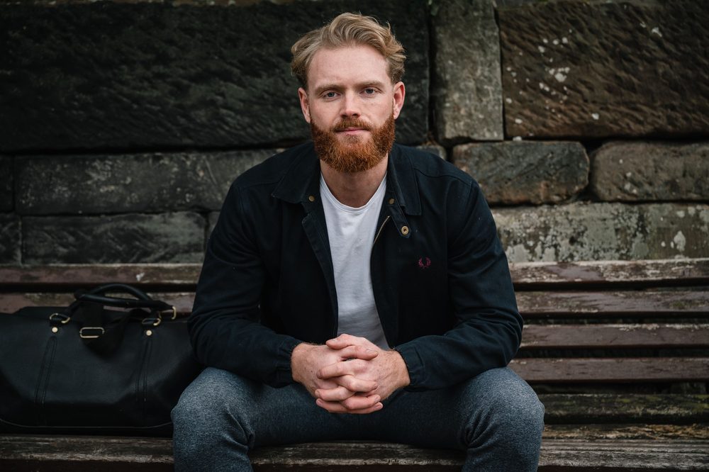 Dan Martin sitting on a bench against a stone wall in Castlefield